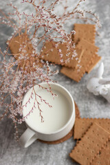 A white ceramic mug with milk, biscuits and a white ceramic bunny surrounded by small white flowers. A gentle breakfast in a light key