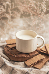 A white mug with milk and dry biscuits, white small flowers, taken from above in close-up. A gentle cozy breakfast