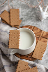 A white ceramic mug with milk, biscuits and a white ceramic bunny surrounded by small white flowers. A gentle breakfast in a light key