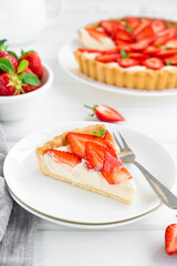 Strawberry tart with custard cream on a plate on a white wooden background. Copy space.