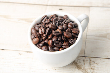 Arabica and Robusta roasted coffee beans in white glass on wooden background cutout