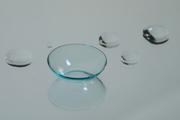 Contact lens and drops of water on white reflective surface