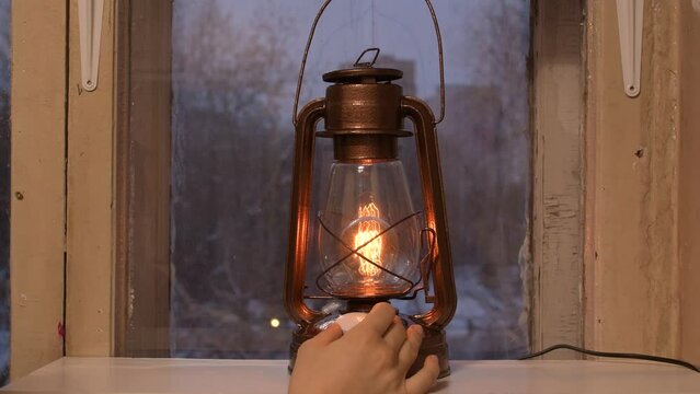 An old oil lamp has been converted into a modern electric lamp with a dimmer. A kerosene lamp is on the window. The concept of reasonable consumption