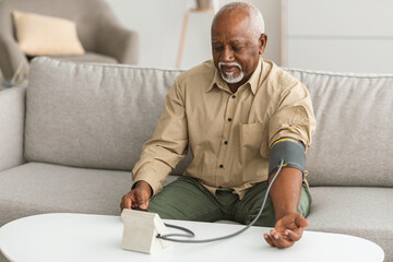 Senior African Man Measuring Arterial Pressure Sitting On Sofa Indoors