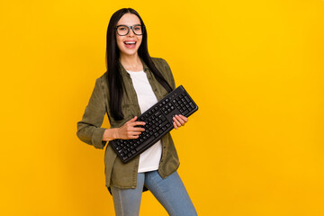 Photo of clever young lady hold keayboard wear eyewear khaki shirt jeans isolated on yellow...