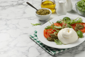 Delicious burrata salad with tomatoes, arugula and pesto sauce served on white marble table. Space for text