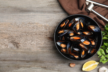 Bowl of delicious cooked mussels with parsley and lemon on wooden table, flat lay