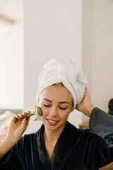 White woman wrapped towel massaging face with jade roller