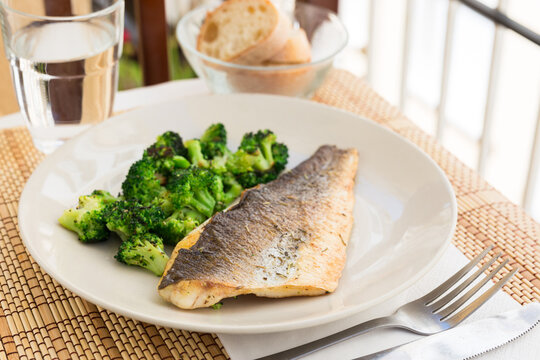 fried fillet of sea bass with garnish of broccoli on black warm stone plate