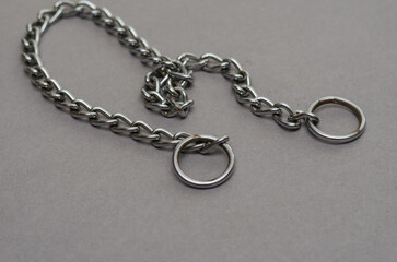 Fototapeta na wymiar Silver metal chain with two rings on a gray background. Tugging