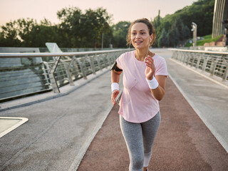 Lifestyle portrait of a confident young female athlete running along the citybridge treadmill at sunrise. Healthy lifestyle concept, cardio workout and jogging activity