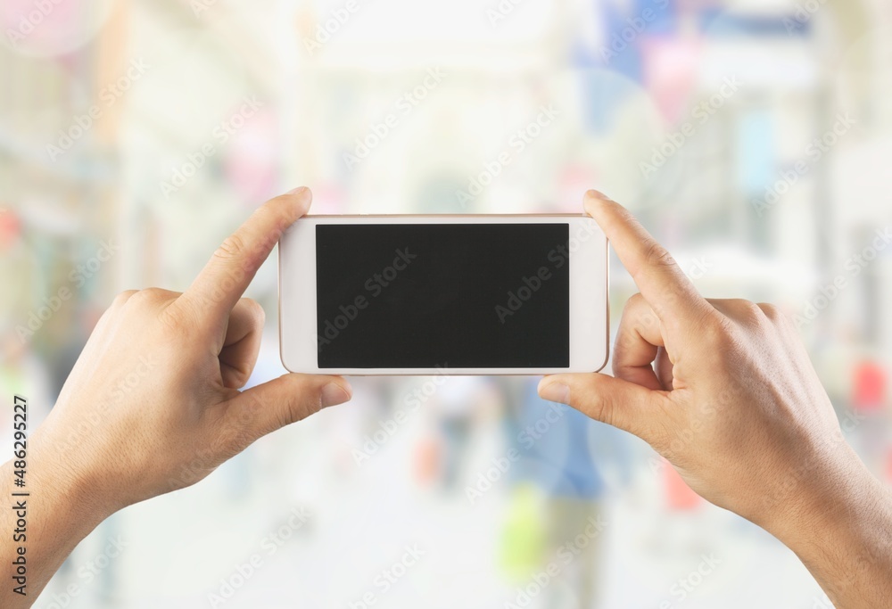 Poster Human hand holding phone with blank screen and cityscape blur background