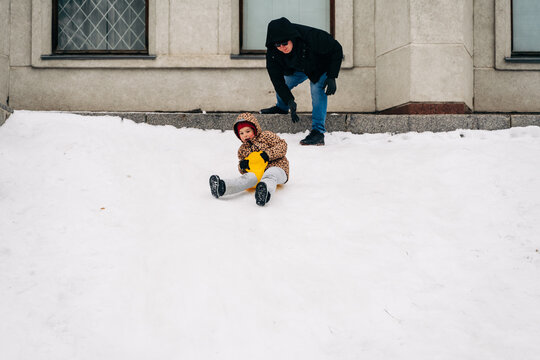 Father pushing kid on snow saucer riding down hill