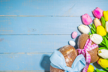 Easter holiday greeting card background, with chocolate easter bunny, eggs, and tulip flowers, on light blue background flatlay frame copy space top view