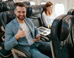 Joyful man with smartphone showing approval gesture in plane