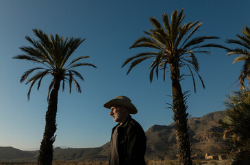 Adult man in cowboy hat on Tabernas desert with palm trees against blue sky. Almeria, Spain