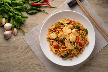 Spicy stir fried instant noodle with sliced chicken breast and thai basil leaves in white plate.top...