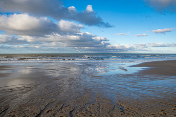Wolken spiegeln sich im Wasser am Strand und Rinnsale im Sand  