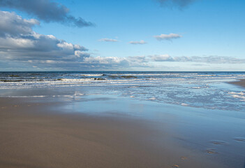 Wolken, Wellen und weißer Schaum am Strand der Nordsee