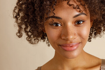 Beautiful lady with curly hairstyle posing against beige wall