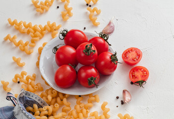 Pasta fusilli and red cherry tomatoes on a white background. Top view. Copy space.