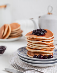 Stack of sweet pancakes close up with jam and berries on a light background. Homemade breakfast concept.