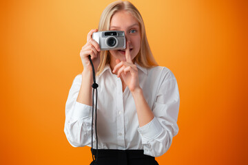 Beautiful teen girl with old photo camera against orange background