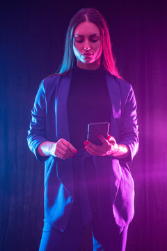 Woman phone . Successful girl with smartphone. Vertical portrait of businesswoman. Modern businesswoman on dark background. Girl looks at screen of phone. Concept of using business applications.