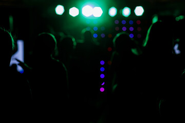 Fototapeta na wymiar cheering crowd in front of bright blue green stage lights. Silhouette image of people dance in disco night club or concert at a music festival.