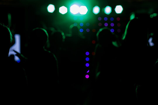 cheering crowd in front of bright blue green stage lights. Silhouette image of people dance in disco night club or concert at a music festival.