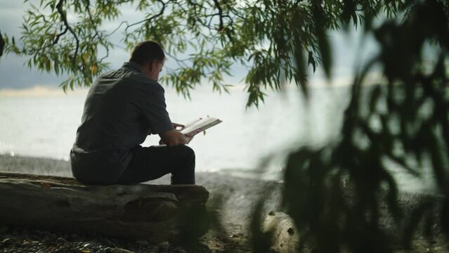 man sitting on a tree reading his bible and praying by beach shore waves