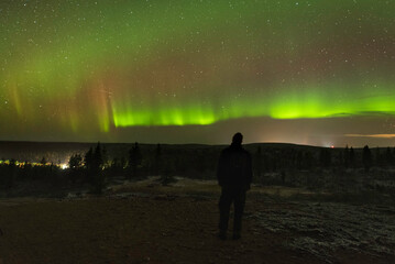 Fototapeta premium Figure in the dark observing night sky with green and purple aurora colors in the sky above the horizon