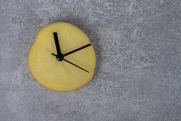 A clock made of potato slices with black hands shows the time on a gray background