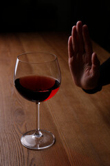 Man refusing to drink red wine at wooden table, closeup. Alcohol addiction treatment