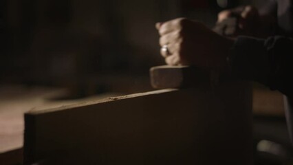 Carpenter working hard using a hand planar, sending wood chips flying into the air in slow motion.