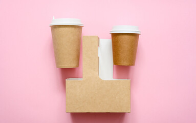 Disposable paper cups and container for carrying cups on a pink background. View from above. Advertisement for food and drink delivery.