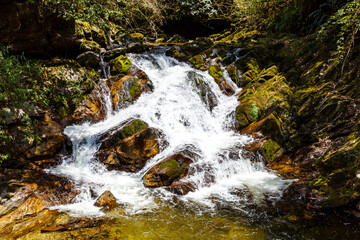 Fototapeta na wymiar Waterfall and big green rocks in the woods next to Burning Lake in Central Bhutan, Asia