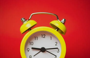 Bright yellow retro alarm clock isolated on red paper background with space for text. Time, minutes, hours concept. The value of time in business and life. Clock showing nine hours and 15 minutes.