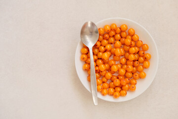 Organic sea buckthorn in a white plate. Layout on a gray table, flat lay. Fresh orange berries in bright sunlight. Natural valuable food supplement.