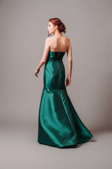 Emerald ball gown. Young lady in long green evening dress. Ginger woman posing in studio. Beautiful...