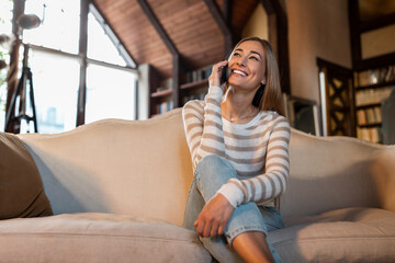 Obraz premium Cheerful woman talking on cellphone sitting on couch