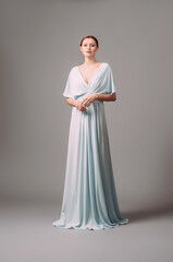 Fototapeta na wymiar Full-length blue bridesmaid dress with flutter sleeves. Effortless festive summer look. Ginger lady in elegant, romantic, tender evening gown. Studio portrait of a young smiling woman.
