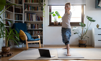 wwoman doing yoga at home online with laptop - warrior 2 pose, Virabhadrasana 2