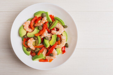 Top view on a plate of salad with avocado, pepper, shrimps, capers on white plate. Mediterranean cuisine.