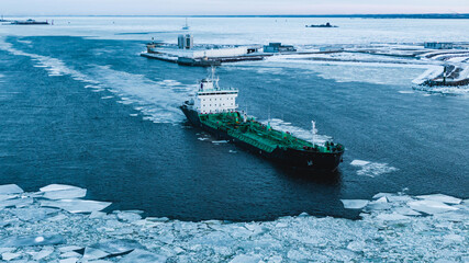 Enormous cargo ship sailing through ocean water with thick layer of broken ice pieces covering...