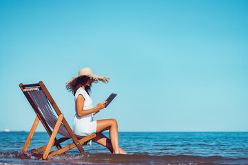 Side view of woman in sunhat who using laptop while lying on the beach chaise longue at the seaside