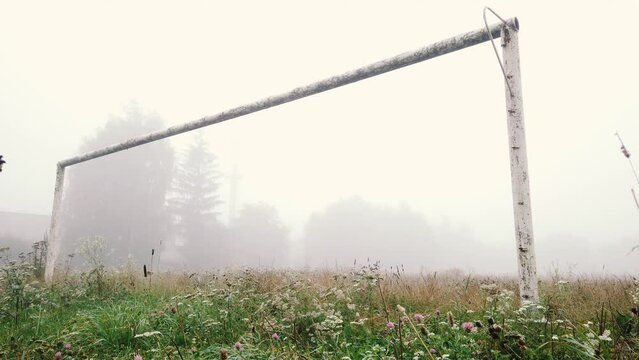 Abandoned football field and old goal post in fall fog. Autumn misty landscape with rusted goalpost and green meadow. Forgotten empty soccer stadium in ghost town