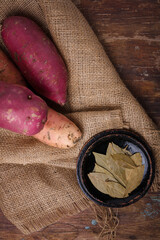 Orange, purple raw sweet potatoes, yam on burlap, wooden rustic table, allspice pepper peas, bay leaves. Farm harvest, organic vegetables, shop local