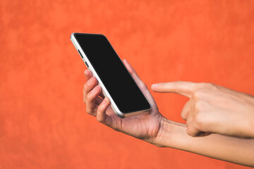 Finger in front of the phone in the girl's hand. Against the background of an orange facade made of decorative plaster.