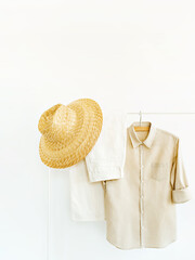 Woman's linen blouse, pants and straw hat in shades of beige with copy space. Rack with female clothes on hangers next to wall. Clothing retails concept. Advertise, sale, fashion. Simplicity concept.